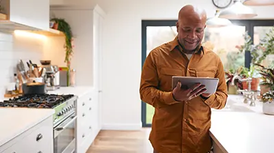 A man standing in his kitchen while using a tablet