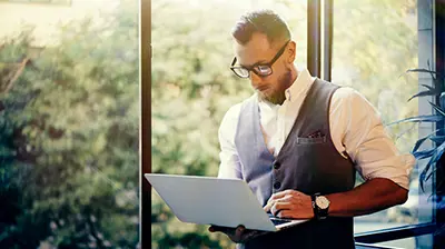 DORIS Man dressed in business casual attire standing by window while using a computer.