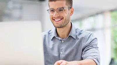 Applied Epic for Salesforce® A man wearing glasses, smiling while using his laptop