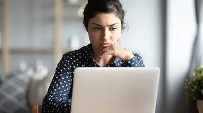 5 Ways to Avoid Spam Filters when Email Marketing A woman in a dark blue polka dot blouse looking seriously at her open laptop.