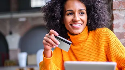Applied Pay: Your New Integrated Digital Payments Solution A woman in an orange turtleneck sweater smiling while holding a credit card in her hand