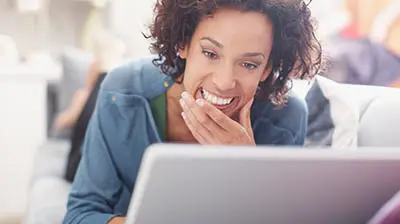 Extending Digital Agency Value to Benefits Brokers A woman smiling with a hand on her chin while looking at a laptop screen.