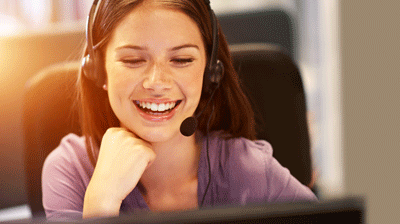 How to Safelist Applied Communications in Your Email Clients A woman wearing a headset while smiling with her hand rested under her chin
