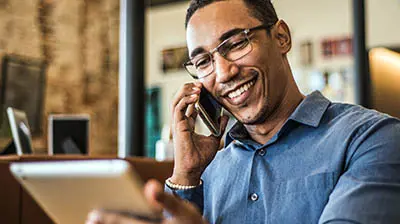 Technology for Your New Insurance Agency A man in a blue button down talking on his cell phone while holding a tablet in the other hand