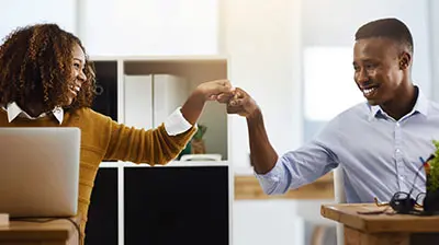 What Does Black History Month Mean to You? A man and a woman fist bumping each other while each sitting at their own desks