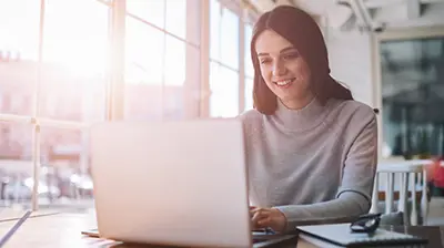 Applied Benefits  A woman in a gray turtleneck, sitting at a desk while using her laptop