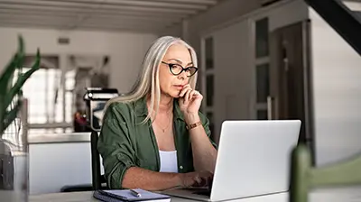 Applied Commercial Lines  A woman sitting at her kitchen table and using a laptop while resting her hand on her chin