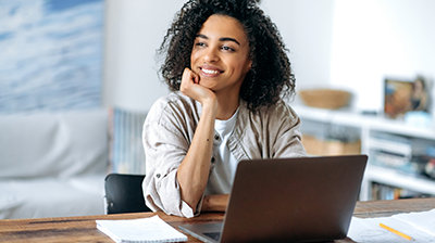 5 Steps to Attract and Retain Top-Tier Insurance Talent A woman sitting at a desk in front of an open laptop, resting her face in her hand while smiling off to the left.