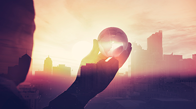 The Digital Revolution of Insurance: Today, Tomorrow and Beyond Silhouette of a man holding a glass ball up to a city skyline with the sun shining through the buildings