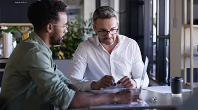 Applied Benefits Designer Two men sitting at a table while having a discussion around an open laptop