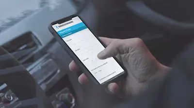 A hand using a smart phone while inside a car.
