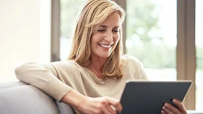 Connected Experience of a Digital Benefits Broker A woman sitting on a chair, smiling while using her tablet