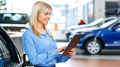 Real Time Mobile Quoting for Insurance Consumers A young woman at a car dealership looking at a tablet
