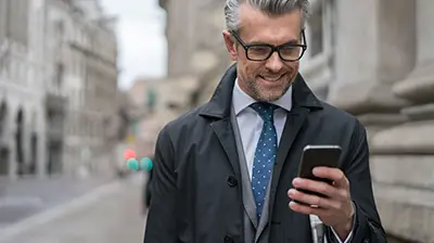 Applied Digital Broker Annual Report A businessman wearing glasses, standing outside, looking at his mobile phone